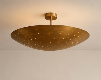 May include: A circular, bowl-shaped ceiling light fitting with a brushed brass finish. The surface features numerous small, perforated holes that allow light to shine through, creating a scattered, star-like illumination effect across the metal.