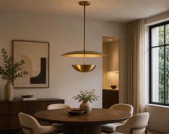 May include: A brass pendant light fitting featuring a large, flat, circular upper shade and a smaller, bowl-shaped lower shade suspended by a central rod. The metallic finish reflects light, creating a warm glow within the dining room space.