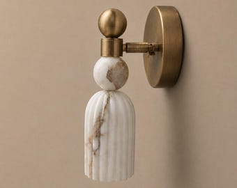 May include: A wall-mounted light fitting with a brass finish and a white marble shade. The fixture features a round backplate, a horizontal arm, and a decorative marble shade with vertical grooves. The marble has brown veining.