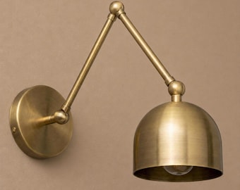 May include: A brass wall lamp featuring an adjustable arm and a domed shade. The lamp has a circular base and a visible lightbulb. The design is vintage-inspired and suitable for various interior styles. The measurements are in centimeters.