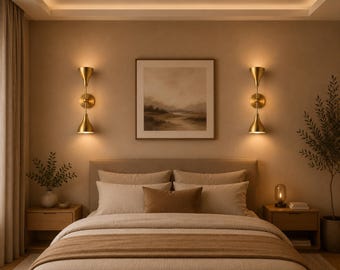 May include: Two gold-toned wall sconces with dual conical shades mounted symmetrically on a beige wall, flanking a square framed landscape print above a bed with neutral-coloured bedding, pillows, and two wooden bedside tables.