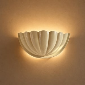 May include: A cream-colored wall sconce with a scalloped, shell-like design. The light fixture is mounted on a beige wall, and the light source is emitting a warm glow. The sconce has a glossy finish and a decorative, elegant style.