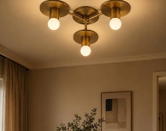 May include: A ceiling-mounted light fitting featuring three brass-toned metal arms extending from a central hub. Each arm ends in a circular brass plate with a downward-facing cylindrical socket holding a spherical white glass light bulb.