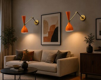 May include: Two wall-mounted lamps featuring vibrant orange, dual-cone shades with small perforated details along the rims. The fixtures are supported by adjustable brass-toned metal arms that extend from circular wall plates, emitting warm light.