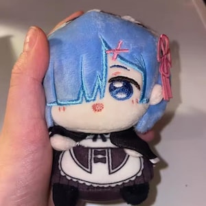 May include: A plush doll featuring a character with blue hair and large blue eyes. The doll is wearing a maid outfit with a black top and a white apron. A pink bow is attached to the doll's hair. The doll is approximately 5 inches tall.