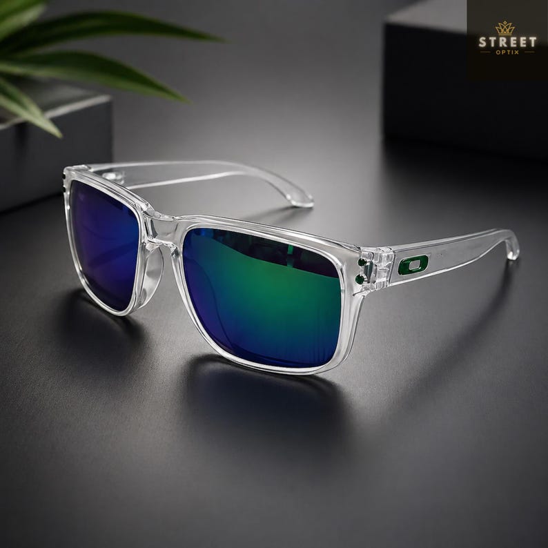 May include: Clear-framed sunglasses with mirrored lenses reflecting blue and green hues. The sunglasses have a square shape and a small green logo on the temples. The brand name "STREET OPTIK" is visible in the upper right corner.