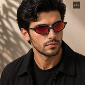 Peut inclure: Lunettes de soleil ovales noires avec verres rouges. Les lunettes ont un design moderne. L'image montre une personne portant les lunettes, avec une chemise noire.