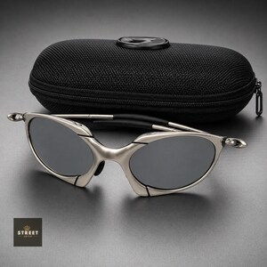 Peut inclure: Lunettes de soleil &agrave; monture argent&eacute;e avec verres gris fonc&eacute; et &eacute;tui noir. Les lunettes ont un design &eacute;l&eacute;gant et moderne avec une monture incurv&eacute;e et un pont noir. L'&eacute;tui est zipp&eacute; et a une surface textur&eacute;e.