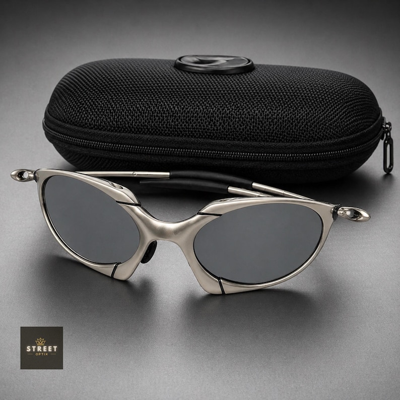 Peut inclure: Lunettes de soleil &agrave; monture argent&eacute;e avec verres gris fonc&eacute; et &eacute;tui noir. Les lunettes ont un design &eacute;l&eacute;gant et moderne avec une monture incurv&eacute;e et un pont noir. L'&eacute;tui est zipp&eacute; et a une surface textur&eacute;e.