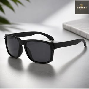 May include: Black sunglasses with a square frame. The sunglasses have dark lenses and a matte finish. The arms of the sunglasses are straight and have a slight curve at the end. The sunglasses are sitting on a light-colored surface.