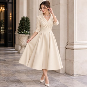 May include: A cream-coloured midi dress featuring a wide lapel collar, a wrap-style bodice with pleated detailing, three-quarter length sleeves, and a full, flared skirt that falls below the knees. The garment is solid in colour with a smooth finish.