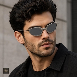 Peut inclure: Lunettes de soleil ovales avec une monture argent&eacute;e et des verres fonc&eacute;s. Les lunettes de soleil ont un design &eacute;l&eacute;gant et moderne. L'image pr&eacute;sente une personne portant les lunettes.