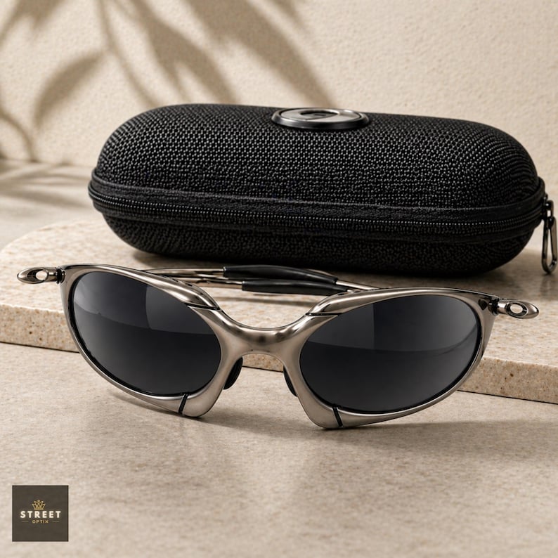 Peut inclure: Des lunettes de soleil &agrave; monture argent&eacute;e et verres fonc&eacute;s sont pos&eacute;es devant un &eacute;tui noir zipp&eacute;. Les lunettes de soleil ont un design &eacute;l&eacute;gant et moderne. L'&eacute;tui a un embl&egrave;me circulaire sur le dessus. Le logo "STREET OPTICS" est en bas &agrave; gauche.