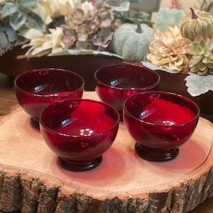 May include: Four ruby red glass dessert bowls on a wooden slice. The bowls are round and have a footed base.