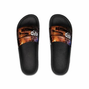 May include: Pair of black slide sandals. The top of each sandal features a design with a silhouette of a person, a cityscape, and the text "KFD EST. 1885" in white. The sandals have a black sole and a white stripe.