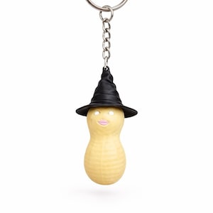 May include: A novelty keychain featuring a peanut-shaped figure wearing a black witch hat. The peanut has a painted face with pink lips and eyes. The keychain includes a silver-colored ring and chain.