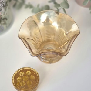May include: An antique amber glass vase with a ruffled edge and a round flower frog. The vase features a pedestal base and etched vertical lines. The flower frog is round with several holes for arranging flowers.