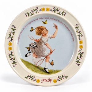 May include: A round ceramic plate featuring a central illustration of a child in a white dress chasing butterflies with a net. The rim is decorated with yellow flowers and green vines. Text reads: A certified plate in the original and only Sarah Stilwell Weber Calendar Collection. July.