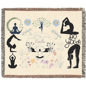 Könnte beinhalten: Eine cremefarbene, gewebte Wohndecke mit schwarzen Silhouetten von Personen in verschiedenen Yoga-Posen, bunten Blumenillustrationen sowie dem Schriftzug "Namaste" und "Do Yoga" und dem Namen "Emilia" in einem dekorativen Wolkenmotiv.