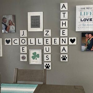 May include: A wall display featuring framed photos, decorative wooden tiles spelling out names, and inspirational quotes. The arrangement includes a heart symbol, paw prints, and a framed shamrock with the text "Lucky in Love."