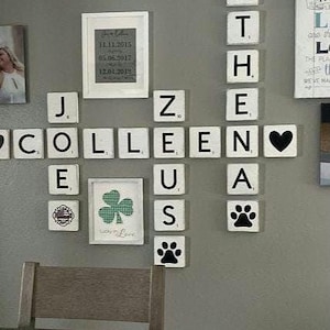 May include: A wall display featuring Scrabble tiles spelling out names and words. The display includes a framed picture with dates and a framed shamrock. Additional tiles show a heart and paw prints.