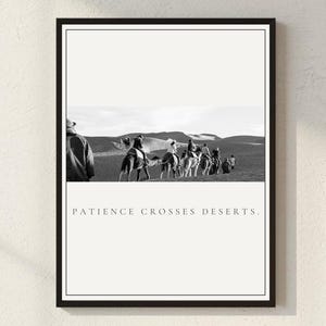 May include: Black and white framed print featuring a desert scene with people riding camels. The print has the text "PATIENCE CROSSES DESERTS" at the bottom. The image is framed in a black border.
