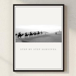 May include: Black and white framed print featuring a desert scene with camels and riders. The image includes the text "STEP BY STEP SURVIVES" in a minimalist design, suitable for home decor.