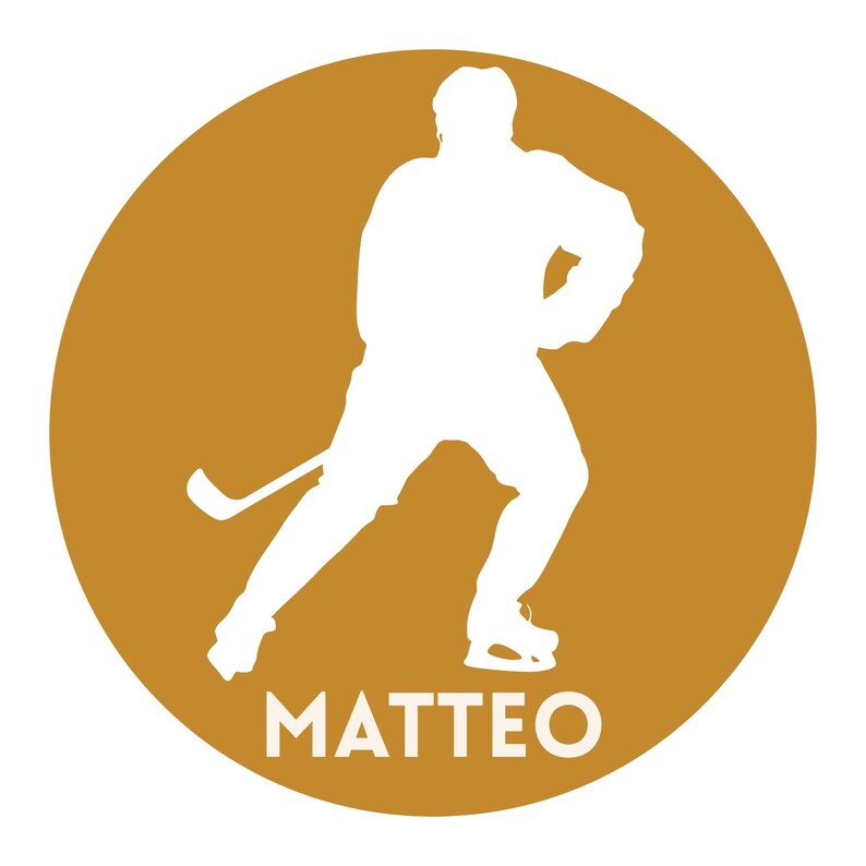 May include: A circular graphic featuring a solid gold background with a white silhouette of a hockey player in a skating stance holding a hockey stick. The name MATTEO is printed in white capital letters at the bottom of the circular design.
