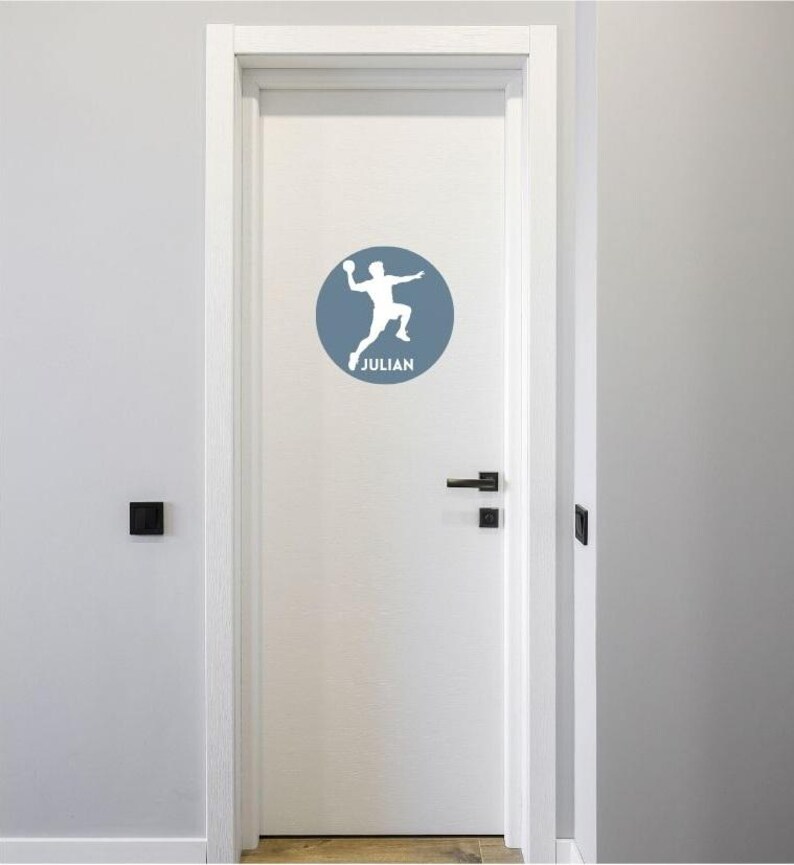 May include: A white door featuring a circular blue decal. The decal displays a white silhouette of a person jumping while holding a ball, with the name JULIAN printed in white capital letters underneath the figure within the blue circle.