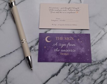 May include: A cream-colored pen with silver accents rests beside two cards. One card has text that reads "No pressure - just thought I'd say hi." The other card is purple with the text "THE SIGN A sign from the universe Destiny."