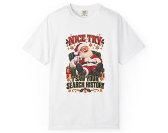 May include: A white short-sleeve t-shirt featuring a graphic of Santa Claus sitting in a green armchair holding a mug. The text above reads NICE TRY and the text below reads I SAW YOUR SEARCH HISTORY, surrounded by small gift boxes and snowflakes.
