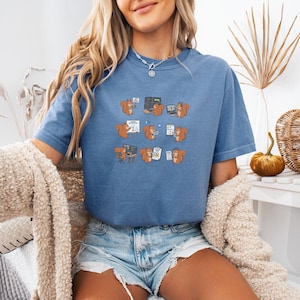 May include: A blue t-shirt with a repeating pattern of cartoon squirrels using computers and working on documents. The squirrels are shown in different poses and expressions. The shirt is made of a soft material.