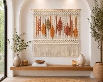 May include: A large macrame wall hanging featuring off-white cord knotted into intricate patterns. The design incorporates several vertical leaf-shaped elements in shades of burnt orange, mustard yellow, and sage green, suspended from a wooden rod.