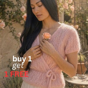 May include: A light pink wrap-style sweater with short sleeves and a tie closure. The image includes the text "buy 1 get 1 FREE". The model is holding a peach-colored rose, with a background of climbing roses.
