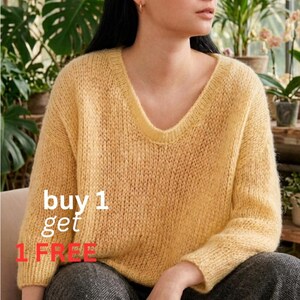 Peut inclure: Une femme porte un pull jaune clair à col en V et à manches longues. Le pull est de couleur unie. Le texte "buy 1 get 1 FREE" est superposé en blanc et rouge.