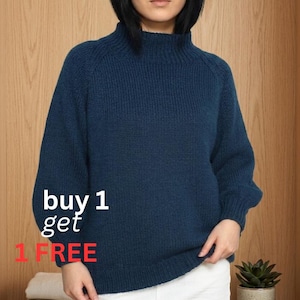 Könnte beinhalten: Eine Frau trägt einen dunkelblauen Rollkragenpullover und einen weißen Rock. Der Pullover hat eine gerippte Textur. Der Text "buy 1 get 1 FREE" ist auf dem Pullover zu sehen. Eine kleine Topfpflanze steht auf einem Regal.