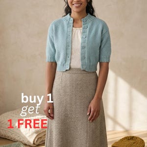 Könnte beinhalten: Eine Frau trägt einen hellblauen Kurzarm-Cardigan über einem weißen Oberteil und einen langen, beigefarbenen Rock. Das Bild enthält den Text "buy 1 get 1 FREE". Zusätzliche Artikel sind ein Stapel Mützen und zwei gefaltete Decken.