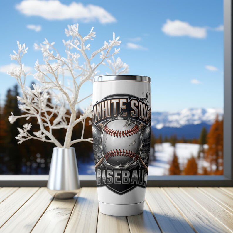 Op de afbeelding: Een witte roestvrijstalen beker met een honkbalontwerp en de tekst "WHITE SOX BASEBALL". De honkbal is wit met rode stiksels. De beker heeft een zilveren rand en een witte basis.