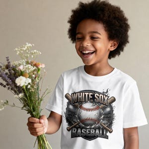 Op de afbeelding: Wit T-shirt met een honkbalontwerp. De afbeelding bevat een honkbal, knuppels en stadionlichten, met de tekst "WHITE SOX BASEBALL". Het shirt wordt gedragen door een lachend kind.