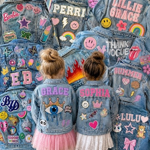 Op de afbeelding: Een collectie blauwe spijkerjacks versierd met diverse kleurrijke stoffen patches, waaronder namen zoals Perri, Lillie Grace, Summer, Lulu, Grace en Sophia, naast iconen zoals regenbogen, smileys, hartjes en sterren.