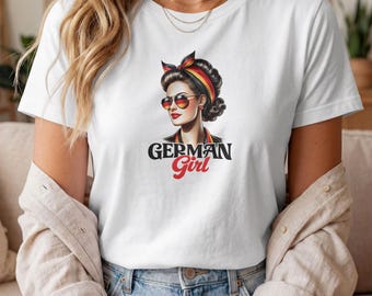 Puede incluir: Una camiseta blanca con una ilustración gráfica de una persona de cabello oscuro que lleva un pañuelo y gafas de sol, ambos con los colores negro, rojo y dorado de la bandera alemana. El texto GERMAN Girl está impreso debajo de la ilustración.
