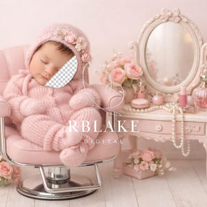 Könnte beinhalten: Ein schlafendes Baby in einem rosa Strick-Outfit und -Hut, verziert mit floralen Akzenten, ruht in einem rosa Stuhl. Im Hintergrund befindet sich ein Schminktisch mit Spiegel, Parfümflaschen und Perlen, mit rosa Rosen.