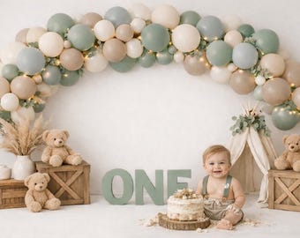 Sfondo per servizio fotografico "Cake Smash" con arco di palloncini a tema orsacchiotto in stile boho, colore neutro verde salvia e beige, per il primo compleanno di un maschietto.
