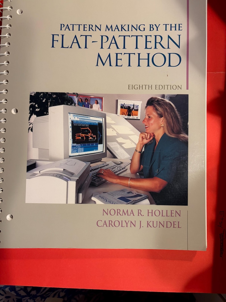 Pu&ograve; includere: Un libro di testo a spirale intitolato Pattern Making by the Flat-Pattern Method, Eighth Edition, di Norma R. Hollen e Carolyn J. Kundel. La copertina presenta una fotografia di una persona che usa un computer per progettare modelli.
