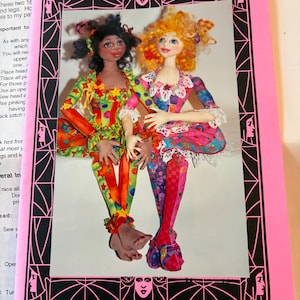 May include: A pattern booklet titled Dominique and Lesley, Soul Mates featuring two 16-inch jointed dolls. The cover shows a doll with dark skin and colorful star-patterned clothing next to a doll with orange hair and pink patterned clothing.