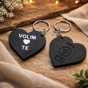 May include: Two black heart-shaped keychains with silver keyrings. One keychain has the words "VOLIM TE" and a white heart. The other has the Spotify logo and the letters "NFC".