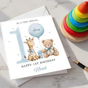May include: A white greeting card featuring a large light blue number one, a watercolor illustration of a giraffe and a teddy bear with blue bows, a light blue balloon, and the text TO A VERY SPECIAL Son HAPPY 1ST BIRTHDAY Noah.