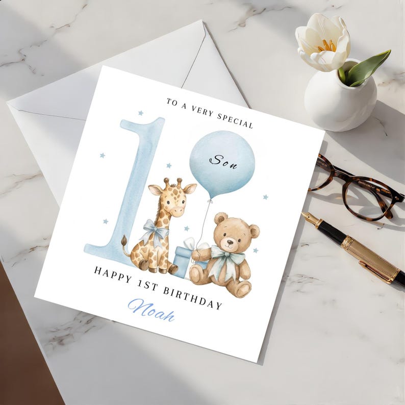 May include: A square birthday greeting card featuring a large light blue number one, a watercolor giraffe, a teddy bear, a blue balloon, and a gift box. The text reads TO A VERY SPECIAL Son, HAPPY 1ST BIRTHDAY, and the name Noah in blue script.