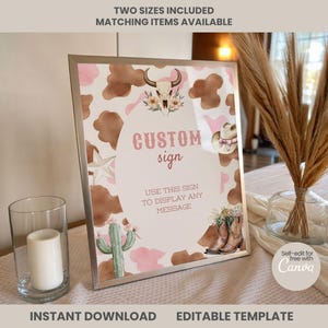May include: A rectangular silver-framed sign featuring a cow print and pink background with illustrations of a bull skull, cowboy hat, cactus, and boots. The text reads CUSTOM sign and USE THIS SIGN TO DISPLAY ANY MESSAGE in a western-style font.