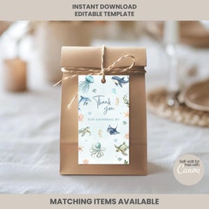 Puede incluir: Una bolsa de regalo de papel marrón con una etiqueta atada con hilo. La etiqueta tiene un diseño de acuarela de criaturas marinas y el texto "Thank you for swimming by". Las palabras "Instant Download Editable Template" están en la parte superior.